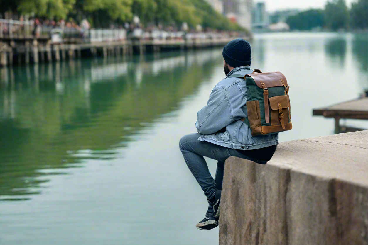 Person sitting by a waterfront with a backpack, looking out over the water.