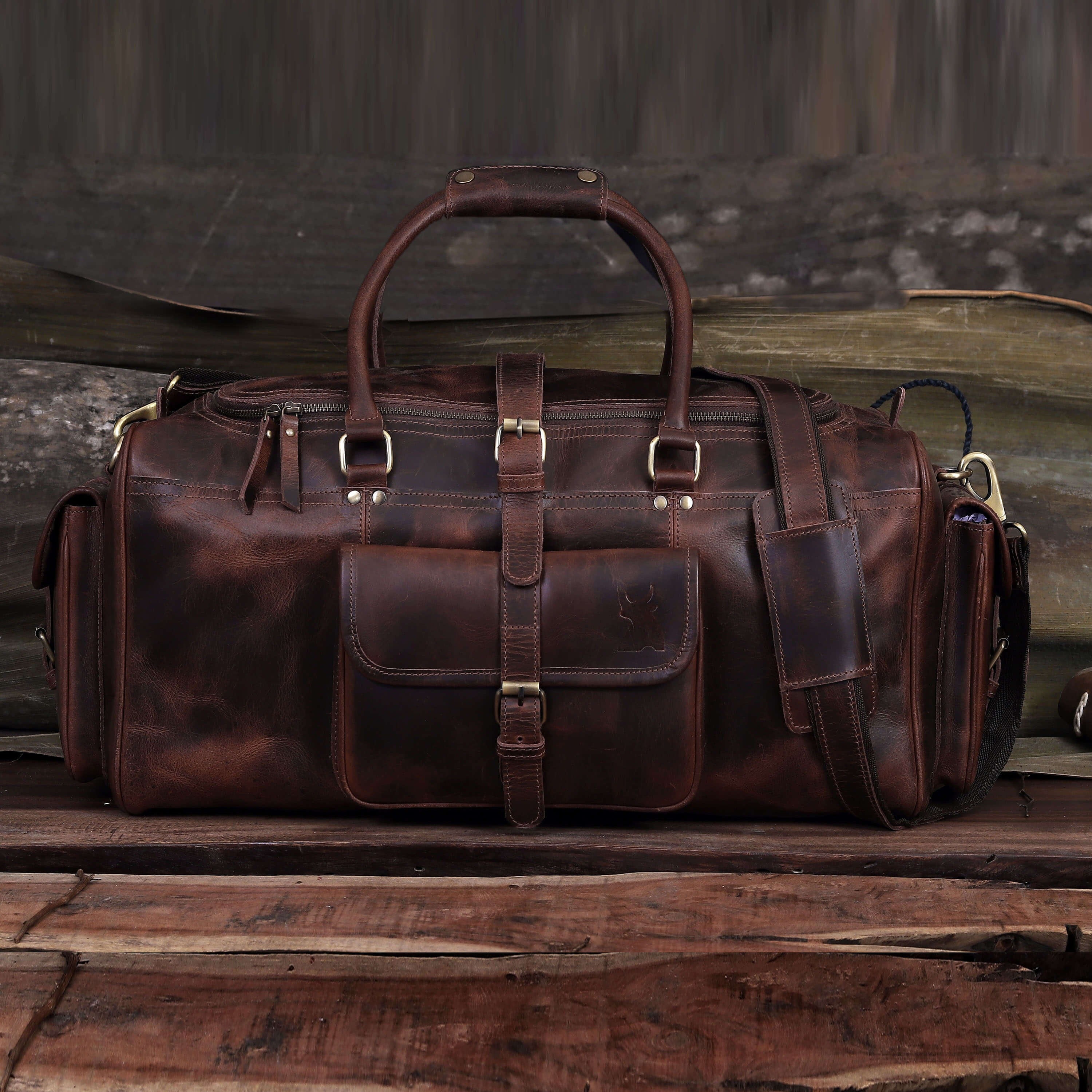 Brown leather duffel bag on a wooden surface with a rustic background