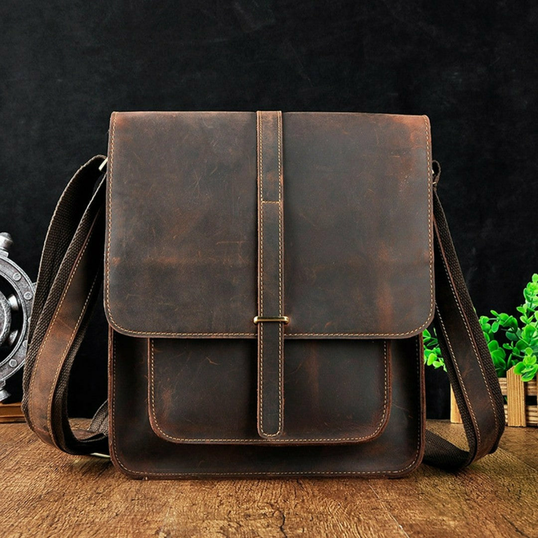 A brown leather crossbody satchel bag with a vintage design, featuring a flap closure over a zipper and a shoulder strap.