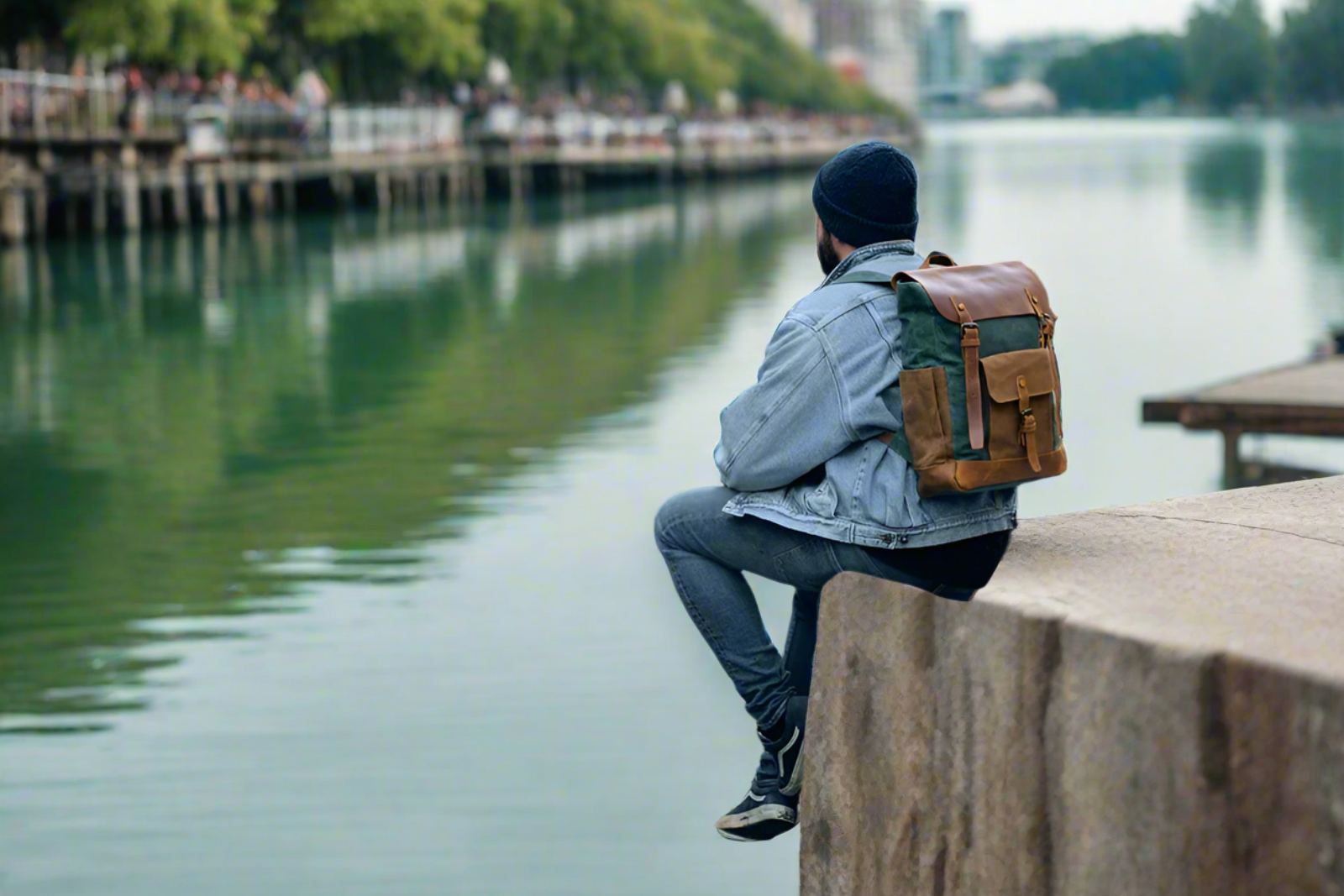 Person sitting by a waterfront with a backpack, looking out over the water.